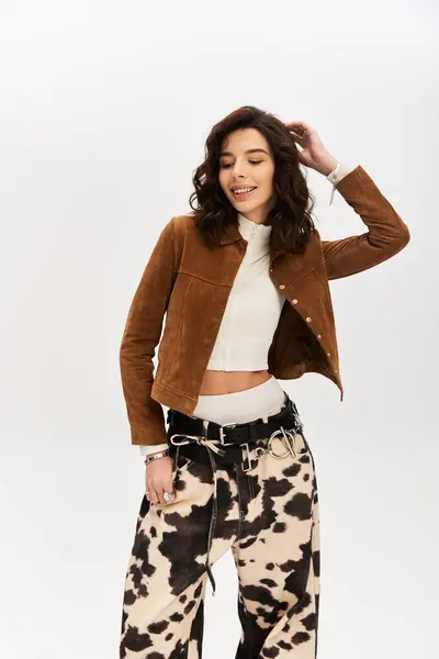 A chic young woman confidently models a fashionable outfit featuring cow print pants in a studio. — Stock Photo