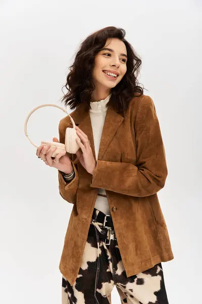 A young woman smiles in stylish cow print pants, holding headphones. — Stock Photo