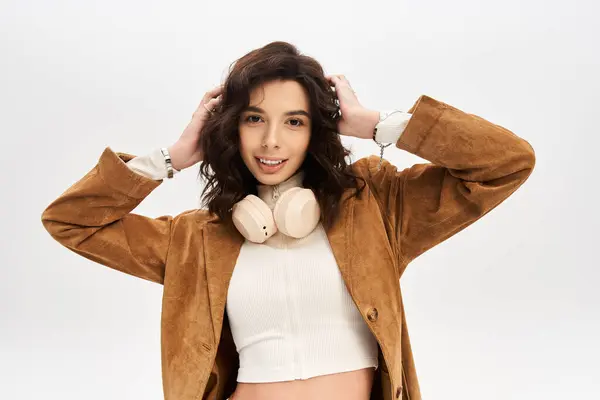 Stylish young woman poses confidently in trendy outfit with headphones a grey background. — Stock Photo