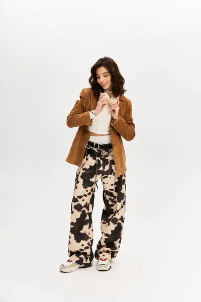 A confident young woman poses in trendy cow print pants against a grey backdrop. — Stock Photo
