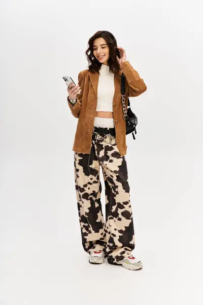 A stylish woman poses confidently in cow print pants while checking her phone. — Stock Photo