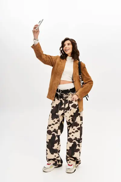 A young woman with a trendy outfit enjoys taking a selfie in a fashionable studio setting. — Stock Photo