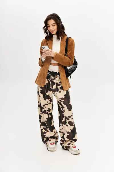 Fashionable young woman engages with her phone while showcasing a chic outfit in studio. — Stock Photo