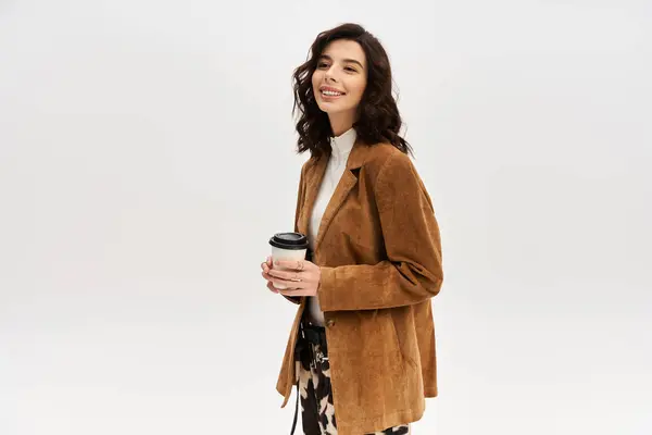 A young stylish woman holds a coffee cup while wearing trendy cow print pants in a studio. — Stock Photo