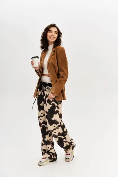 A young woman poses confidently in stylish cow print pants, sipping a drink in the studio. — Stock Photo