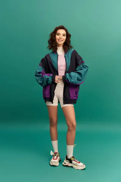 Young woman poses confidently in a chic sporty outfit against a turquoise studio backdrop. — Stock Photo