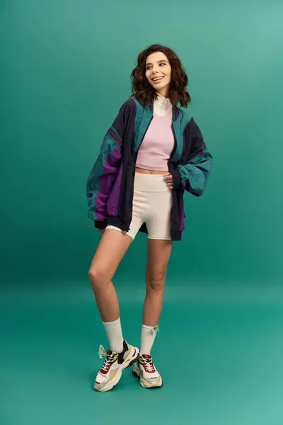 A young woman flaunts her trendy outfit against a vibrant turquoise background. — Stock Photo