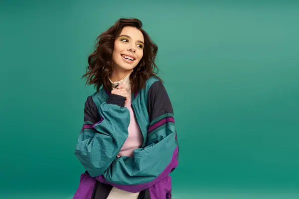 A young woman in a fashionable sporty outfit smiles against a colorful turquoise backdrop. — Stock Photo