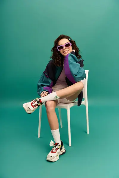 A fashionable young woman in sporty attire poses confidently on a chair in a studio setting. — Stock Photo