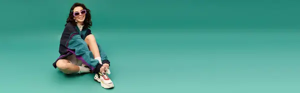 Young woman in fashionable sporty attire relaxes on the floor with a playful smile, banner — Stock Photo
