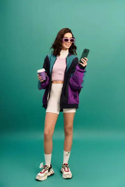 Fashionable young woman wearing sporty attire holds a drink while checking her phone. — Stock Photo