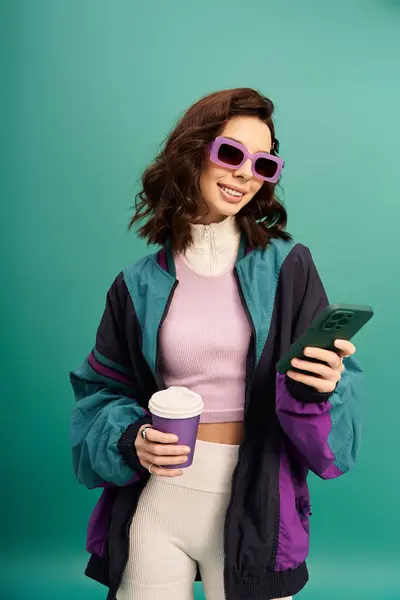 Young woman dressed in a fashionable sporty outfit holds a coffee cup while using her phone. — Stock Photo