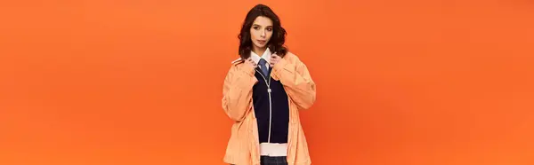 A young woman confidently poses in a chic skirt and jacket against a bright orange backdrop, banner — Stock Photo