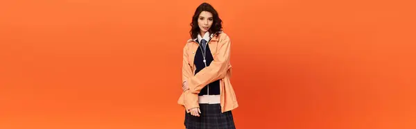 Young woman confidently models a trendy skirt and jacket against a vibrant orange backdrop, banner — Stock Photo