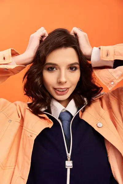 A young woman flaunts her stylish attire against a vibrant orange backdrop. — Stock Photo