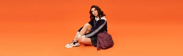 A confident young woman flaunts her chic style in a skirt and jacket against an orange backdrop, banner — Stock Photo
