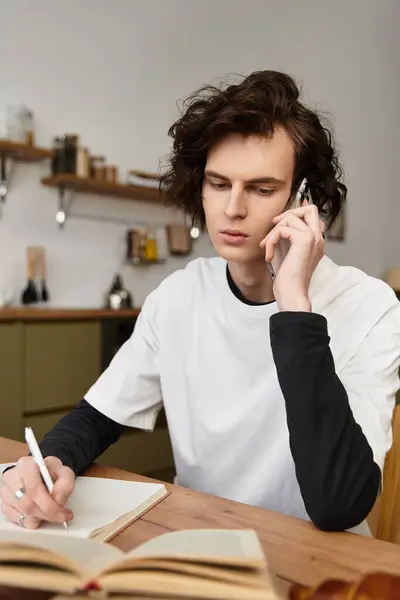 In a cozy home, a young man writes notes while talking on the phone, lost in thought. — Stock Photo