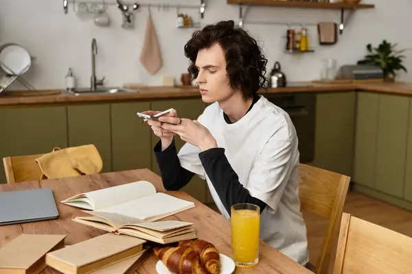 A young man relaxes with his phone, surrounded by books and breakfast. — Stockfoto