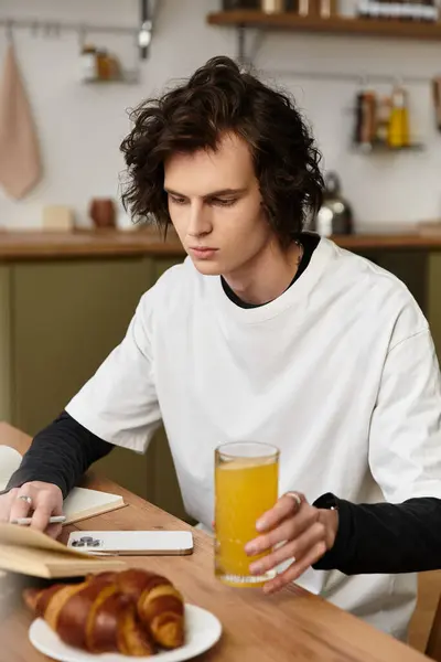 Relaxed young man in comfortable attire savors a drink at a cozy kitchen table with pastries. — Photo de stock