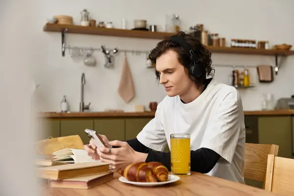 Young man in cozy attire checks his phone while enjoying croissants and juice. — Stockfoto
