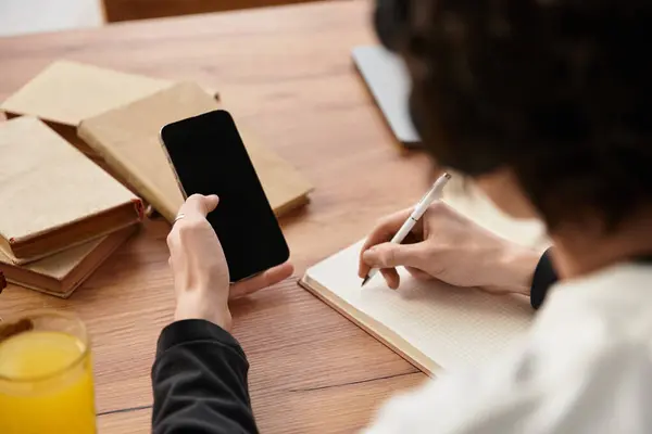 Cozy atmosphere with a young man focused on writing in his notebook and checking his phone. — Stock Photo