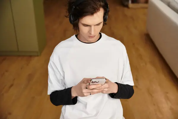 Young man enjoys his leisure time at home, focused on his smartphone while wearing cozy clothes. - foto de stock