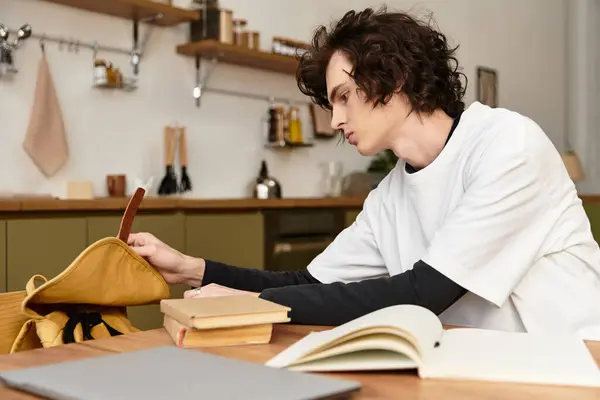 Young man in cozy attire focuses intently on his creative hobby at home, surrounded by books. — Stock Photo