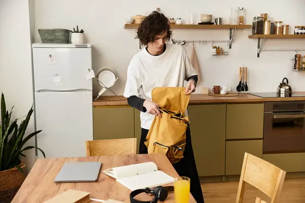 A young man dressed comfortably prepares his backpack in a modern kitchen filled with warmth. — Stock Photo