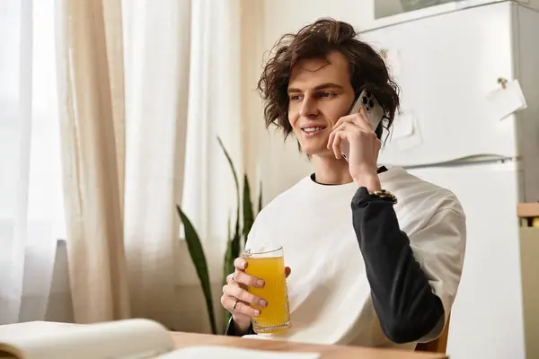 Young man relaxes at home, chatting on the phone with a glass of beverage in hand. — Stock Photo