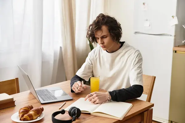 Cozy indoor setting with a young man studying, sipping juice, and savoring croissants. — Stock Photo
