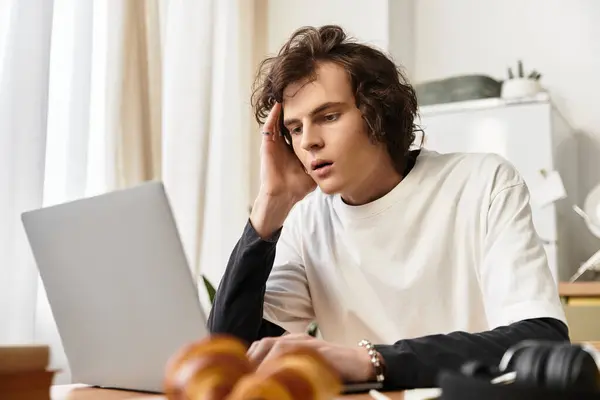 A cozy scene shows a young man on his laptop at home, savoring delicious pastries. — Foto stock