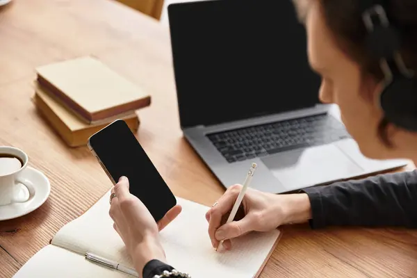 Cozy atmosphere fills the room as a young man writes notes with a phone nearby and a laptop open. — Stock Photo
