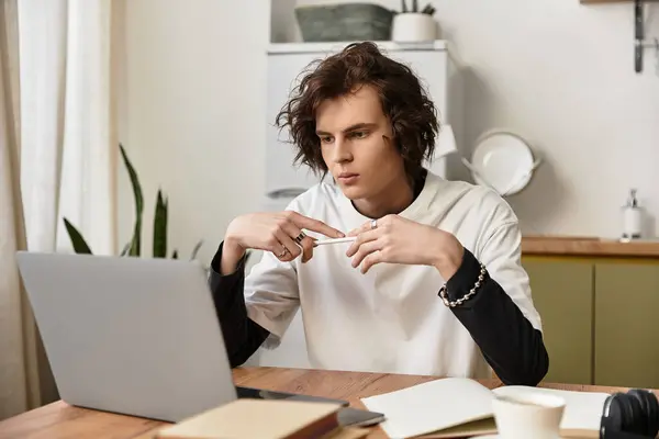 A young man in relaxed clothing concentrates on his laptop at his home workspace. - foto de stock