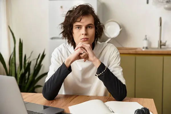 A young man sits thoughtfully at a wooden table in a cozy home setting, dressed comfortably. — Stock Photo
