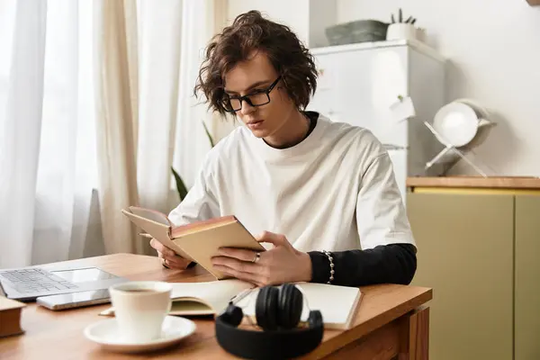 A young man sits at a wooden table, immersed in reading a book while dressed in cozy clothing. — Stock Photo