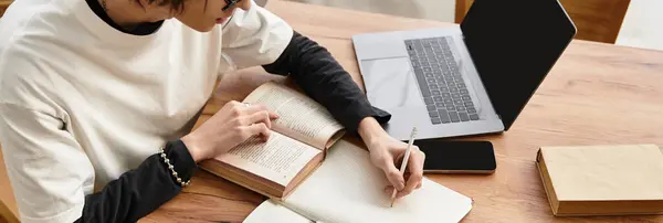 Young man enjoys writing and reading in a cozy home setting with a laptop nearby. — Stock Photo