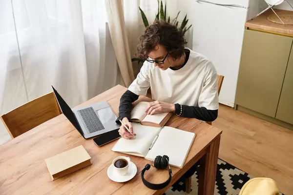 A young man enjoys a peaceful afternoon at home, writing with books and coffee nearby. — Stock Photo