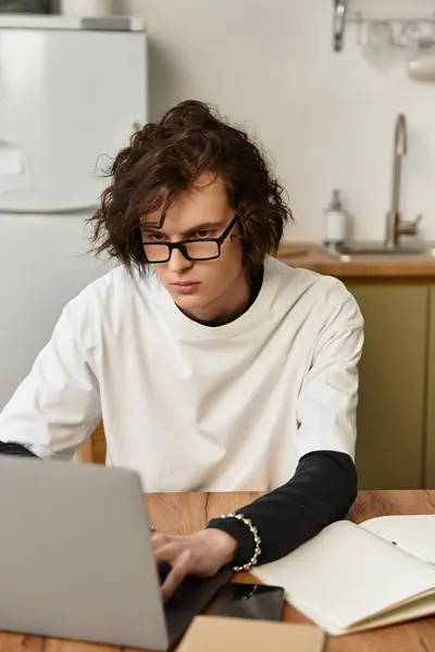 A young man in comfy clothes types on his laptop at a wooden table in a cozy home. — Stock Photo
