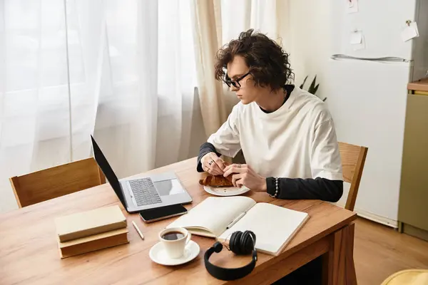 Atmosfera accogliente come un giovane si siede a un tavolo godendo la colazione mentre si lavora con attenzione. — Foto stock
