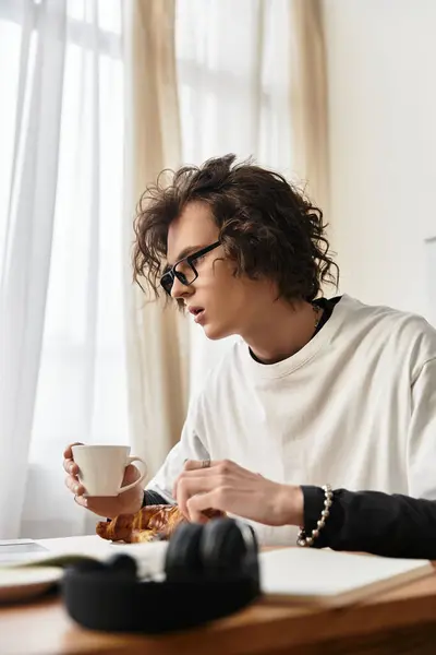 Cozy morning at home features a young man sipping coffee while savoring a pastry in comfort. — Stockfoto