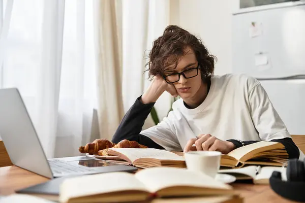 Расслабленный молодой человек в уютной одежде сидит дома и читает книги, наслаждаясь вкусной выпечкой.. — стоковое фото