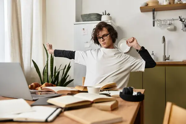 A young man in cozy attire stretches at home, surrounded by breakfast and open books. — Photo de stock