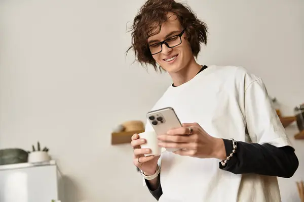 A young man is relaxed at home, dressed in cozy attire while scrolling on his phone. - foto de stock