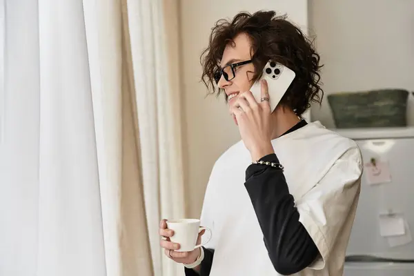 Cozy attire defines the young mans relaxed atmosphere as he chats on his phone, holding a cup. — Stock Photo