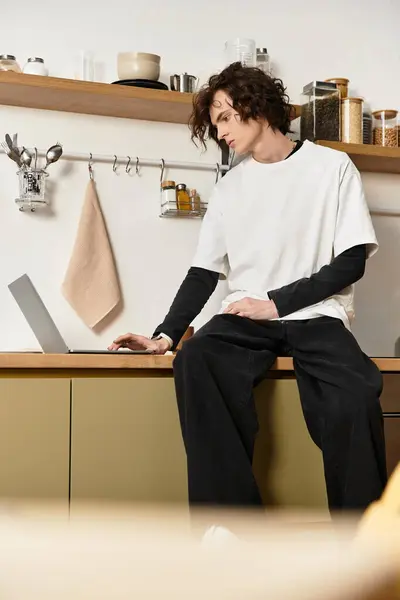 A young man sits comfortably at home, engaged with his laptop while wearing relaxed clothing. — Stock Photo