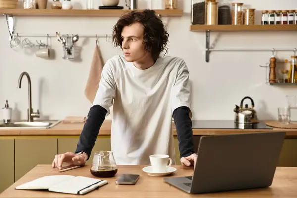 A young man in comfortable clothing stands thoughtfully by a kitchen table, enjoying coffee. — Stock Photo