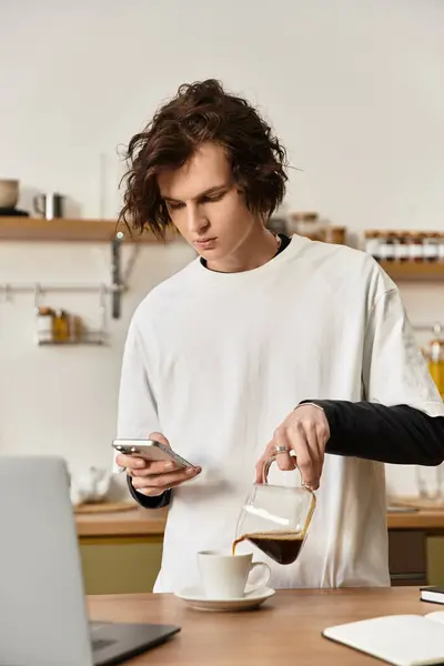 A young man in comfy clothes enjoys a cozy morning at home, sipping coffee and checking his phone. — Photo de stock