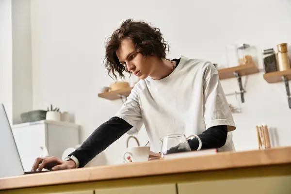 Un joven enfocado en un atuendo cómodo se involucra con su computadora portátil mientras toma café. - foto de stock