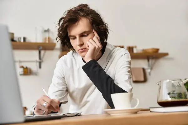 A young man in cozy clothes writes at a wooden table, savoring his coffee. — Stock Photo