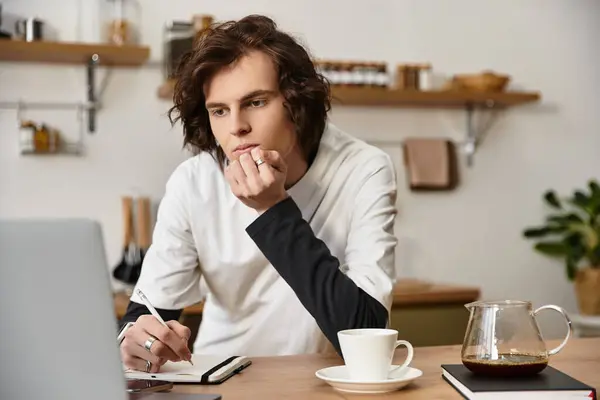 A young man sits at home in comfy clothes, deep in thought as he works on his notebook. — Stock Photo